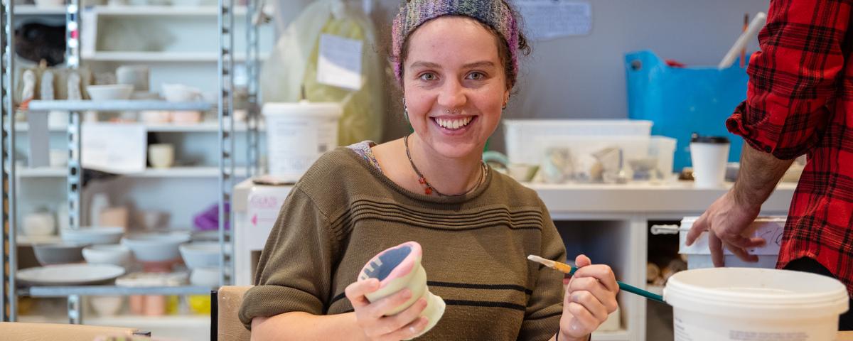 a young woman glazes a pot at a pottery workshop