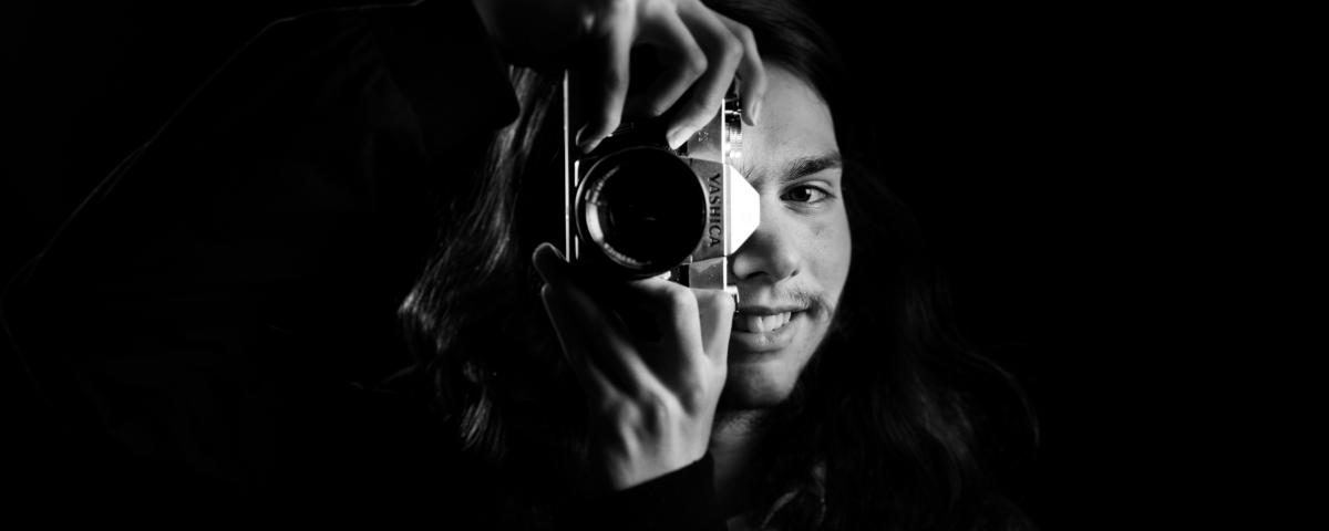 moody black and white portrait of a person smiling behind a camera lens