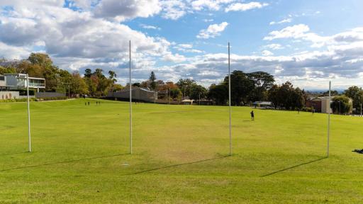 A green sports oval looking directly at 4 AFL goal posts. Trees  line the edge of the oval. 