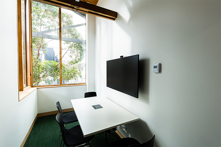 Study room with wall mounted screen, small desk and three chairs.