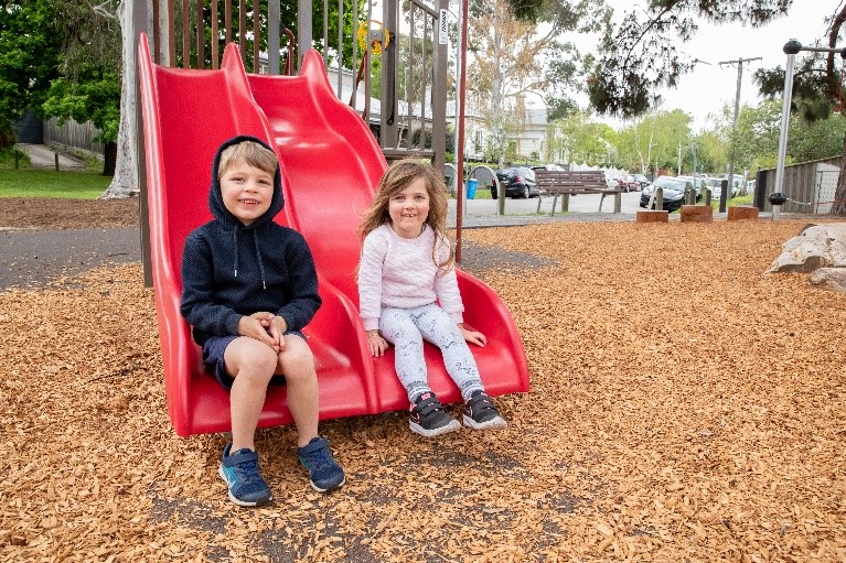 Two children sit on a double slide in a playground
