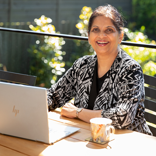 Add Life ambassador Radha Raghunath siting at a table outside with a laptop and a mug.
