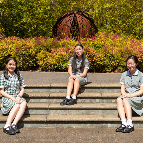 Three high school aged girls Sophie Chiew, Sophia Li and Rino Suwa sitting on the steps in front of the metal ball sculpture in Hawthorn.