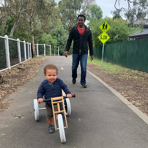 A man walks along his child on a shared bike path while the child rides a tricycle
