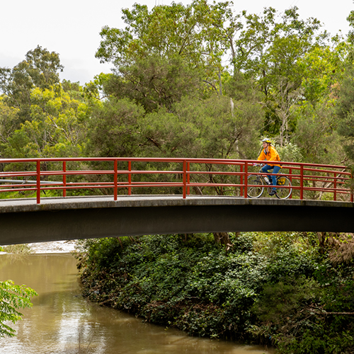 A woman in an orange top rides her bike across a bridge