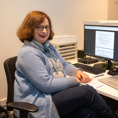 University of the Third Age participant Christine Georgiou sits in front of her computer and smiles at the camera