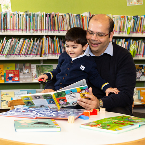 A dad reading a picture book with his child in the library. They both look happy.