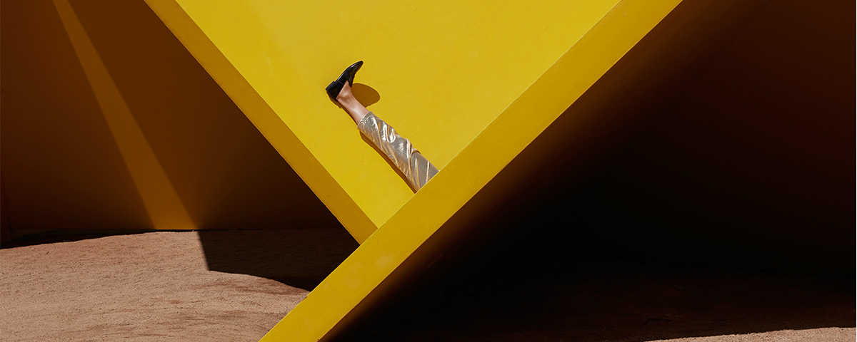A pair of legs laying upwards on a geometric sculpture. The rest of the figure is hidden from view.