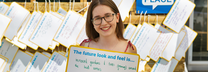 A girl wearing glasses holds a sign and smiles at the camera