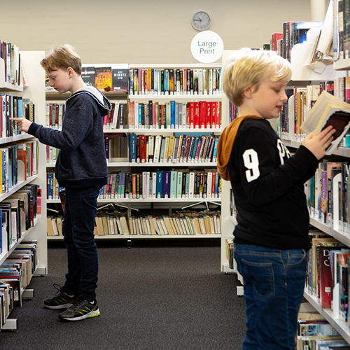 Two young people looking through books on a library shelf