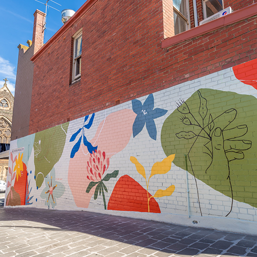 A colourful mural with flowers, an abstract hand and a bird on the side of a building