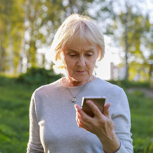 An older woman wearing a lilac top looks at her smart phone