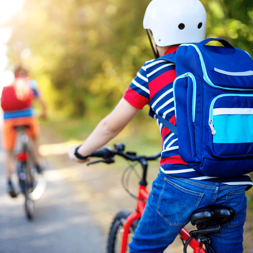 Two children wearing backpacks and helmets riding bicycles