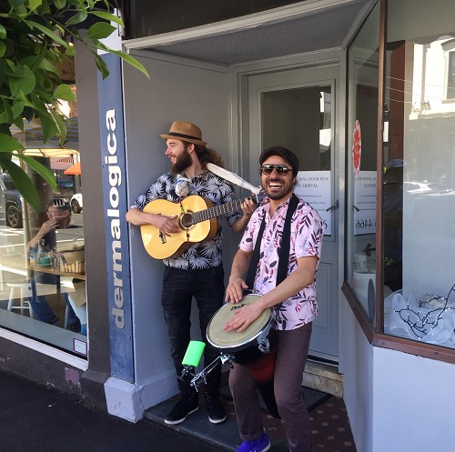 Two musicians standing in a shop doorway playing a guitar and a drum