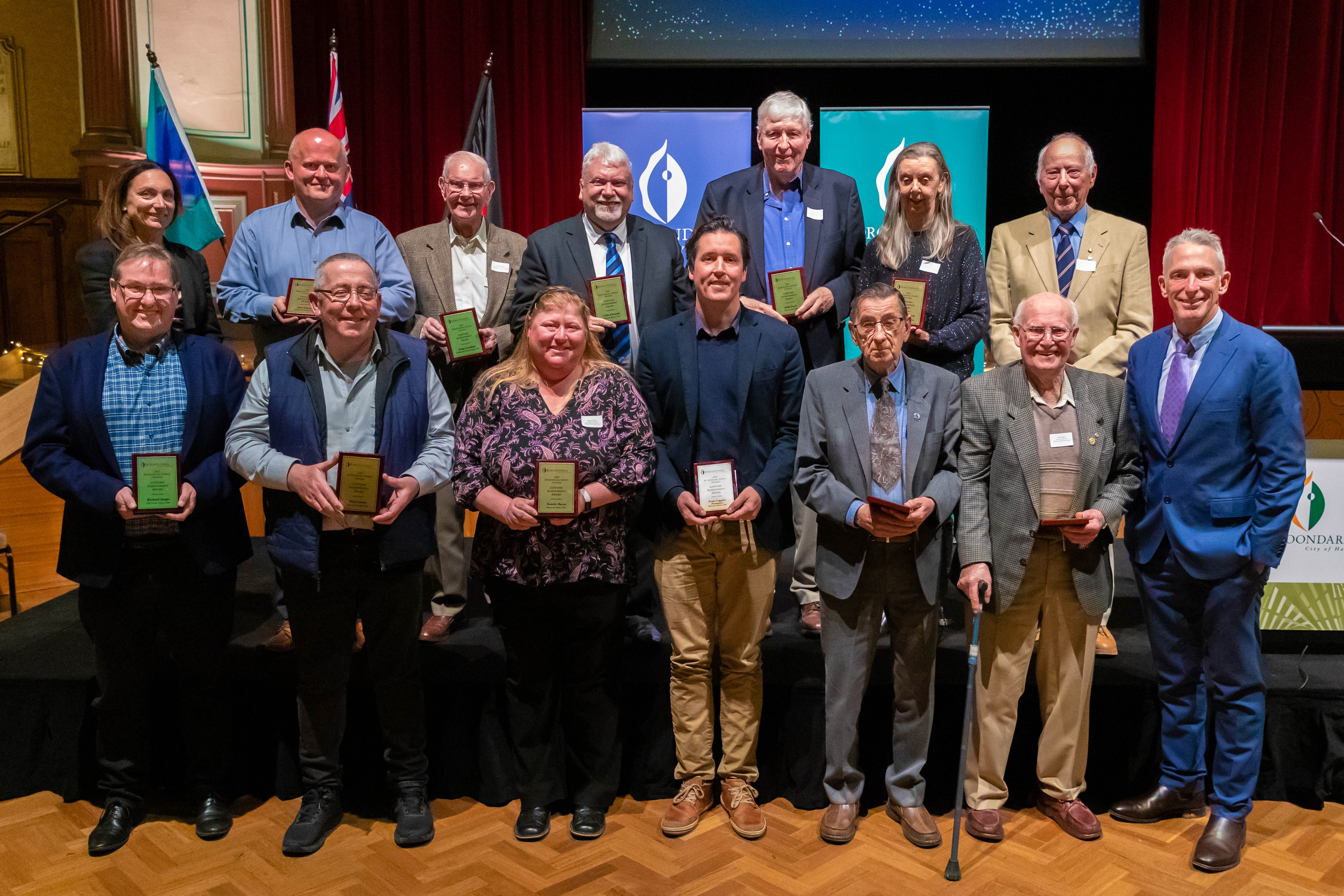14 people standing in 2 rows holding plaques
