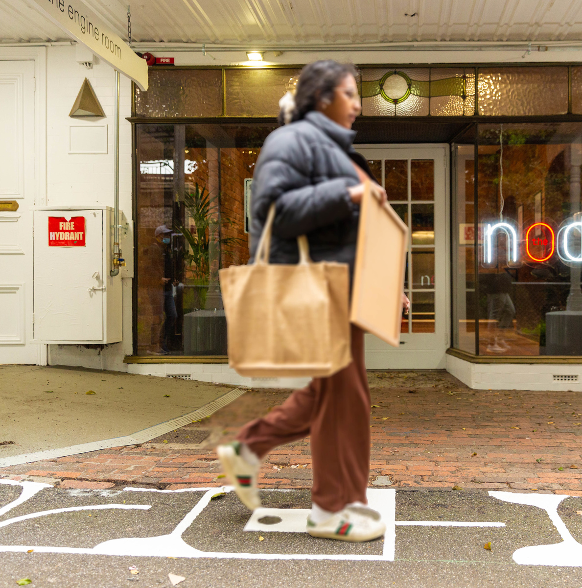 A person carrying shopping bags and walking over white painted footpath art in front of a shop