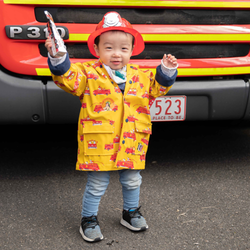 A child in a fireperson suit in front of a fire truck