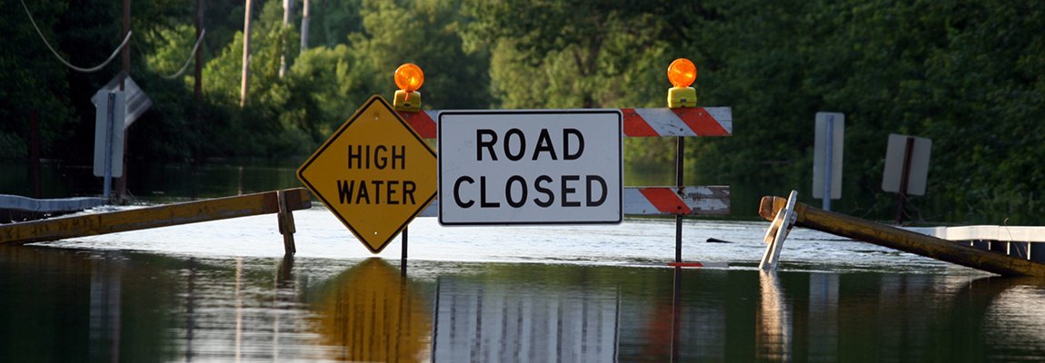 a flooded road with barriers and signs saying 'road closed' and 'high water'