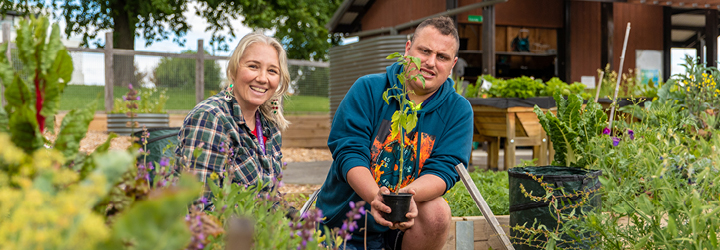 A man and woman holding seedling punnets surrounded by plants