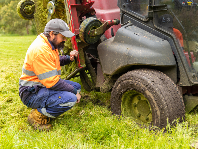 A person looking at a bogged mowing tractor at a park