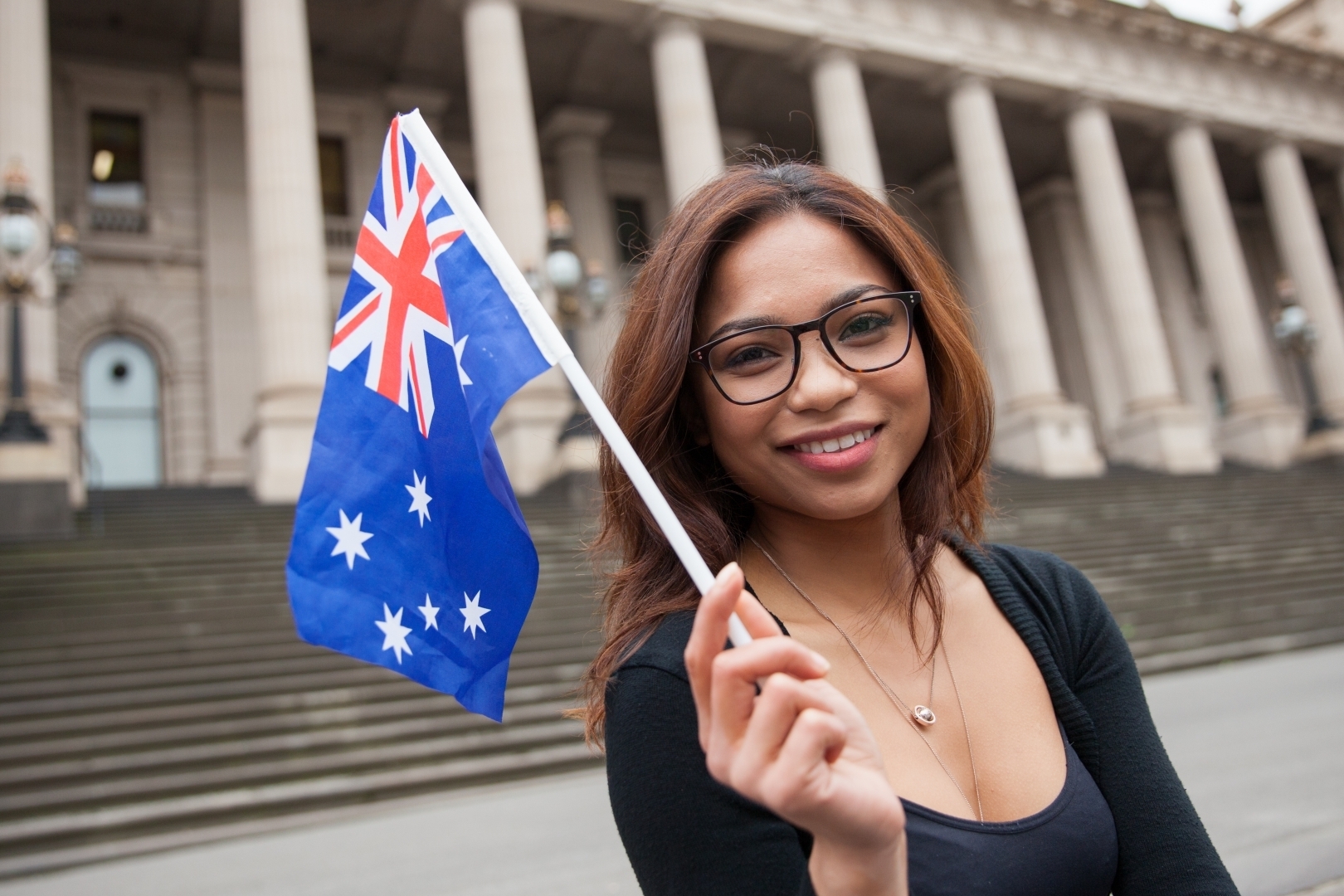 A young person standing outside the Melbourne Parliament building, smiling and holding an australian flag