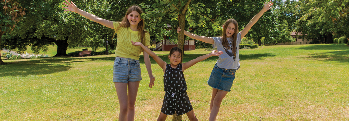 Three young people standing happily around a tree on a sunny day in a park
