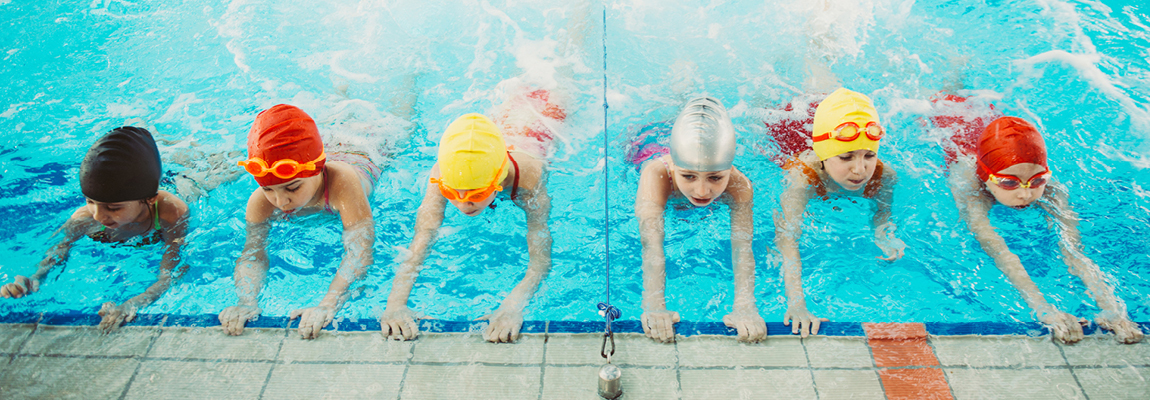 Children in colourful swimming caps kick their legs at an indoor pool