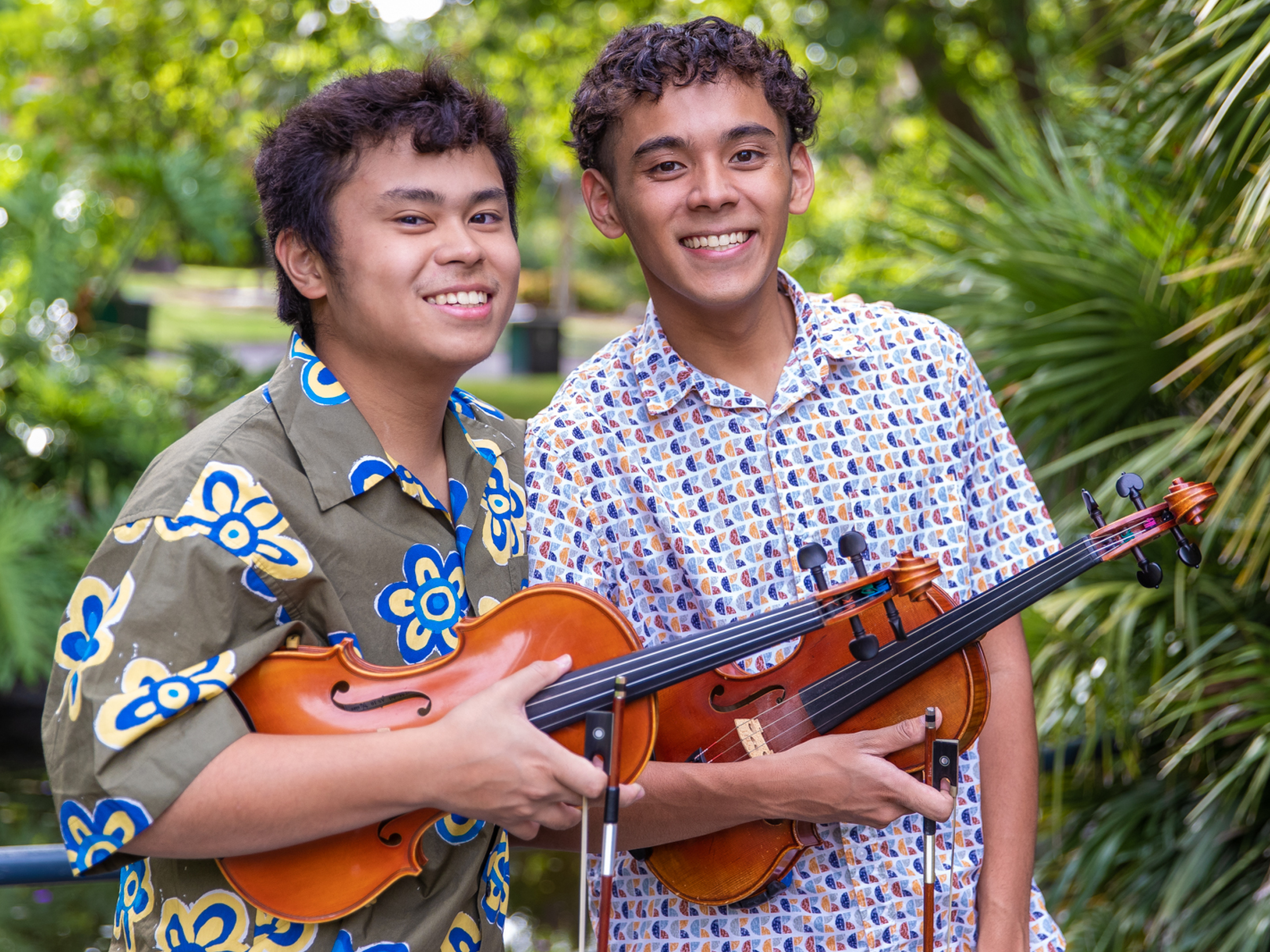 Two young people standing together smiling, each holding a violin