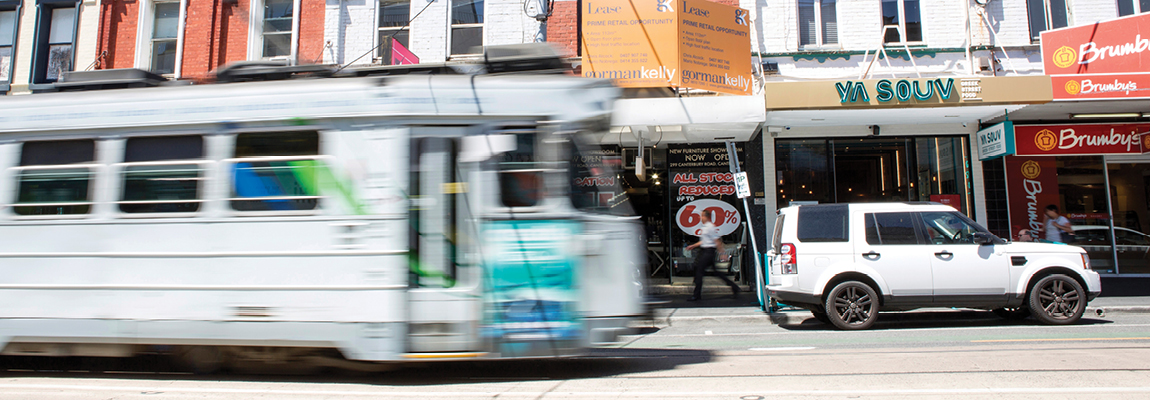 A tram travels past a streetscape of terraced shopfronts