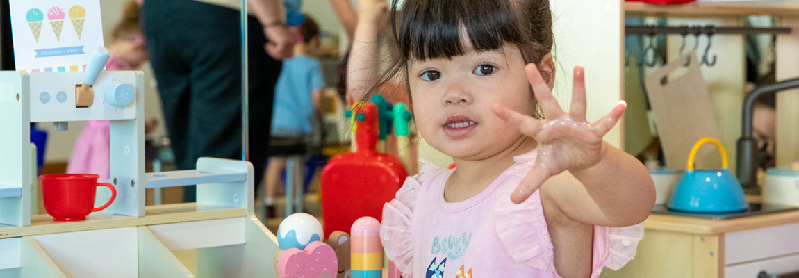 A child shows her open hand in a kindergarten room