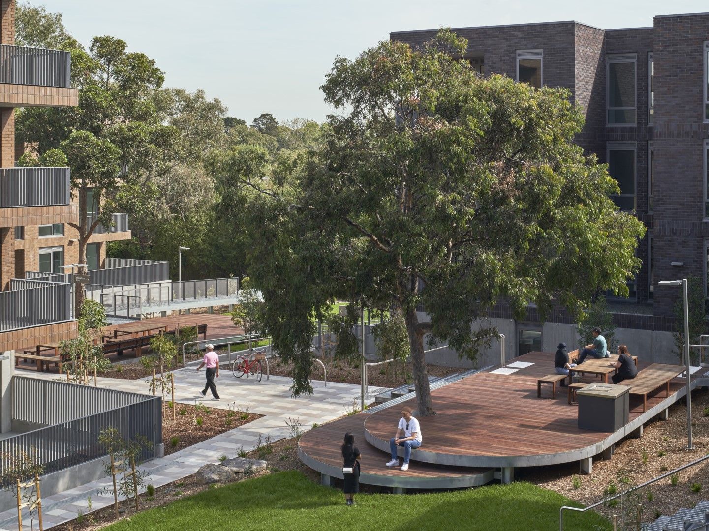 An outdoor area between multi-storey apartments with modern landscaping and recreation areas alongside garden beds and paths