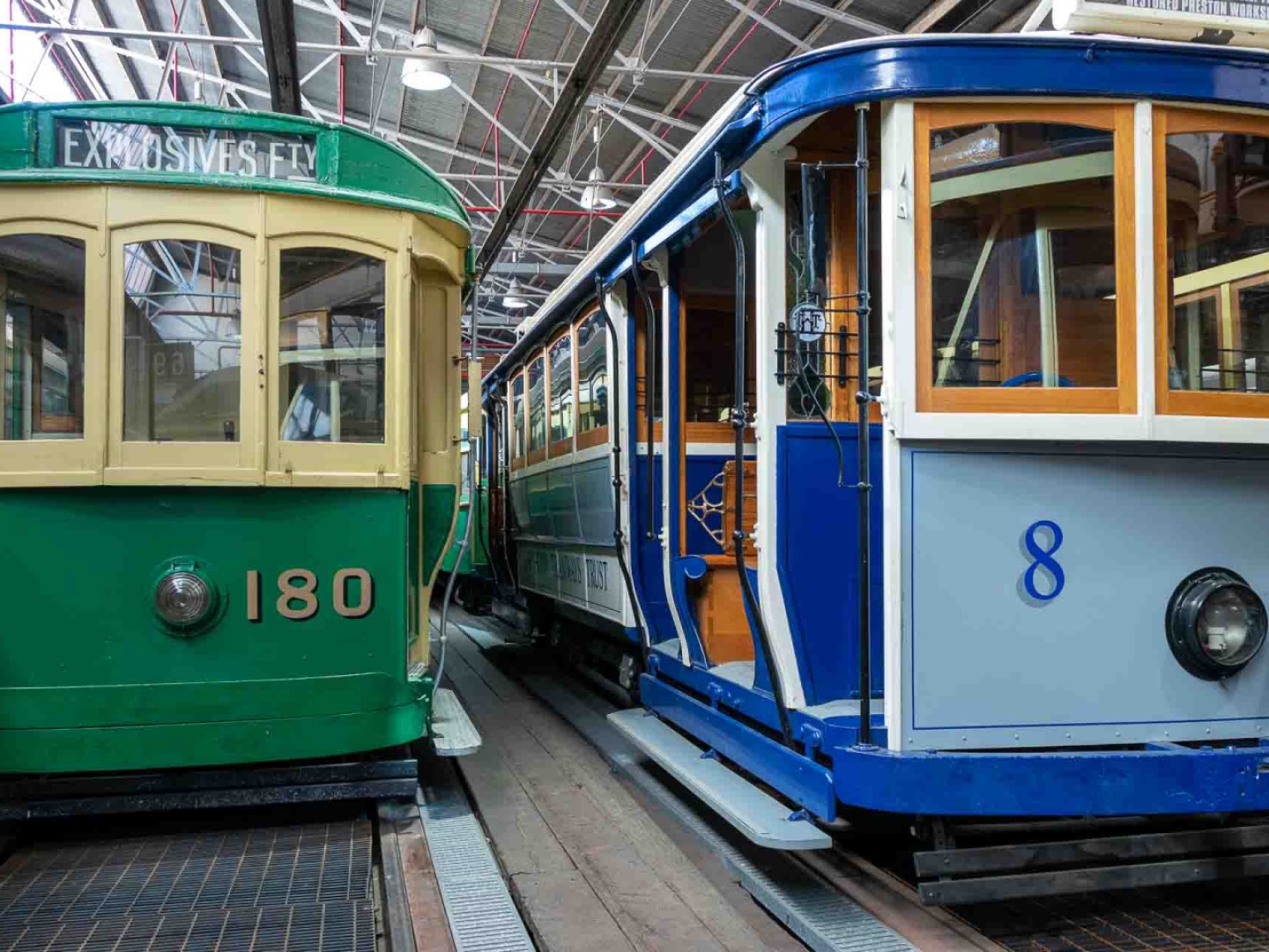Two older style wooden trams with vintage paint, parked next to each other in a warehouse