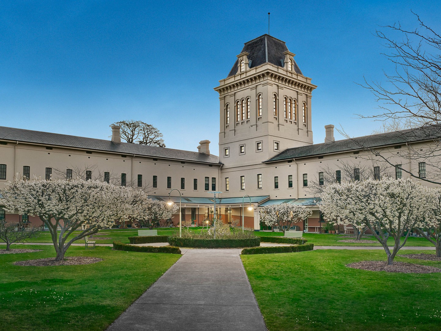 The courtyard of a heritage building with two long wings and a central tower enclosing the green garden full of blossoming trees