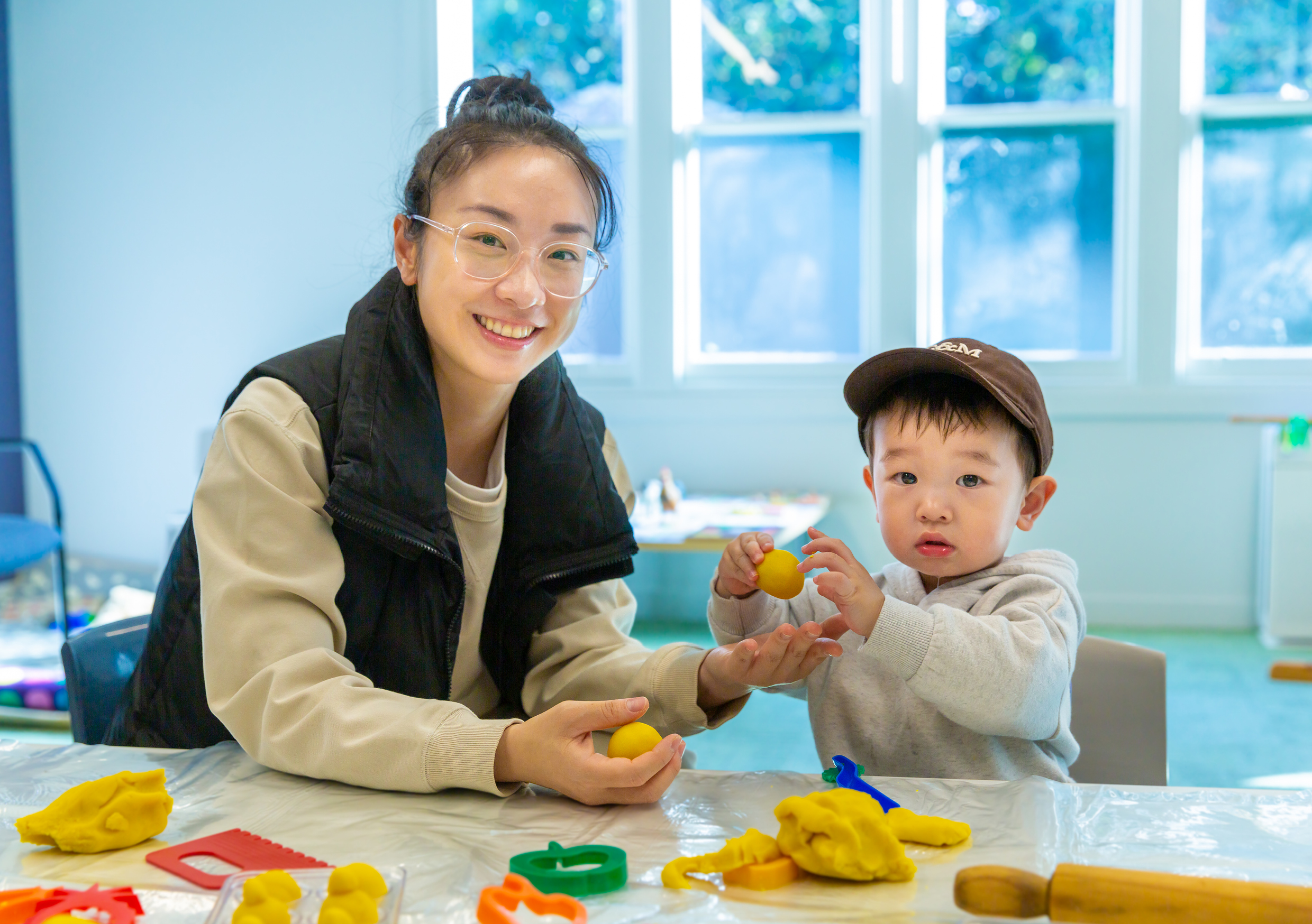 An adult and a young child sitting at a table playing with playdough together