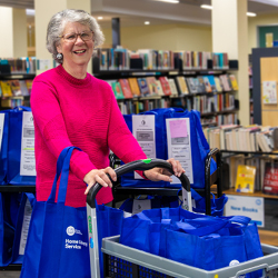 Volunteer Elizabeth Smith pushing trolley among library shelves.