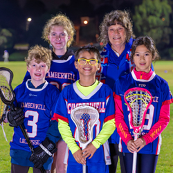 Volunteer Jennie Easson standing near hockey field with 4 young players in blue and pink uniforms.