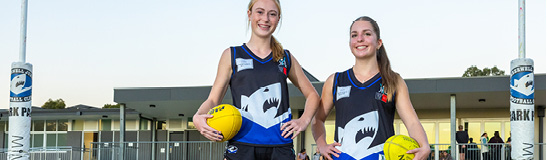 Two women in footy uniforms holding a footy