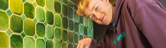 A young person standing next to a bright green tiled wall