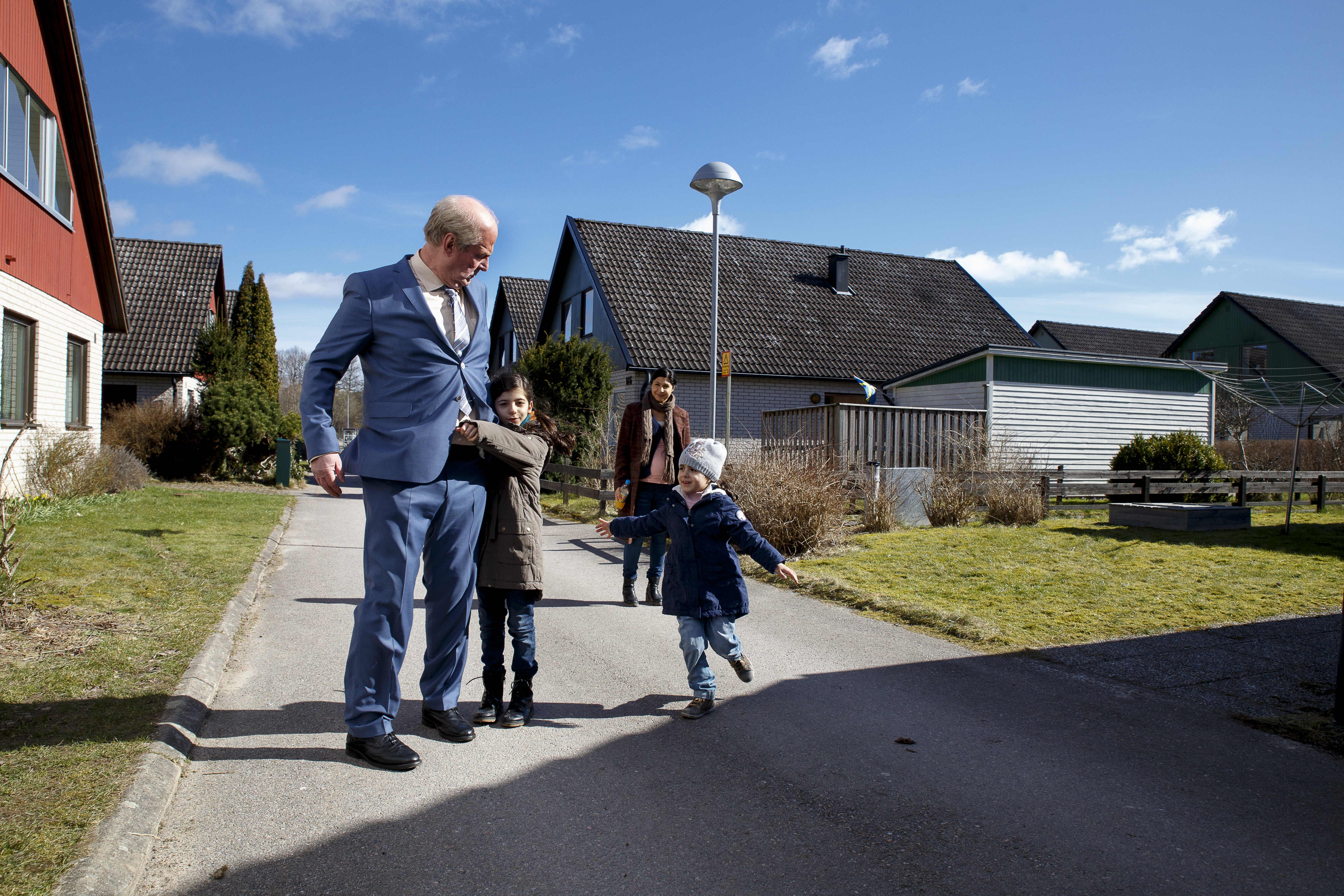 A suited man and 2 children in a driveway