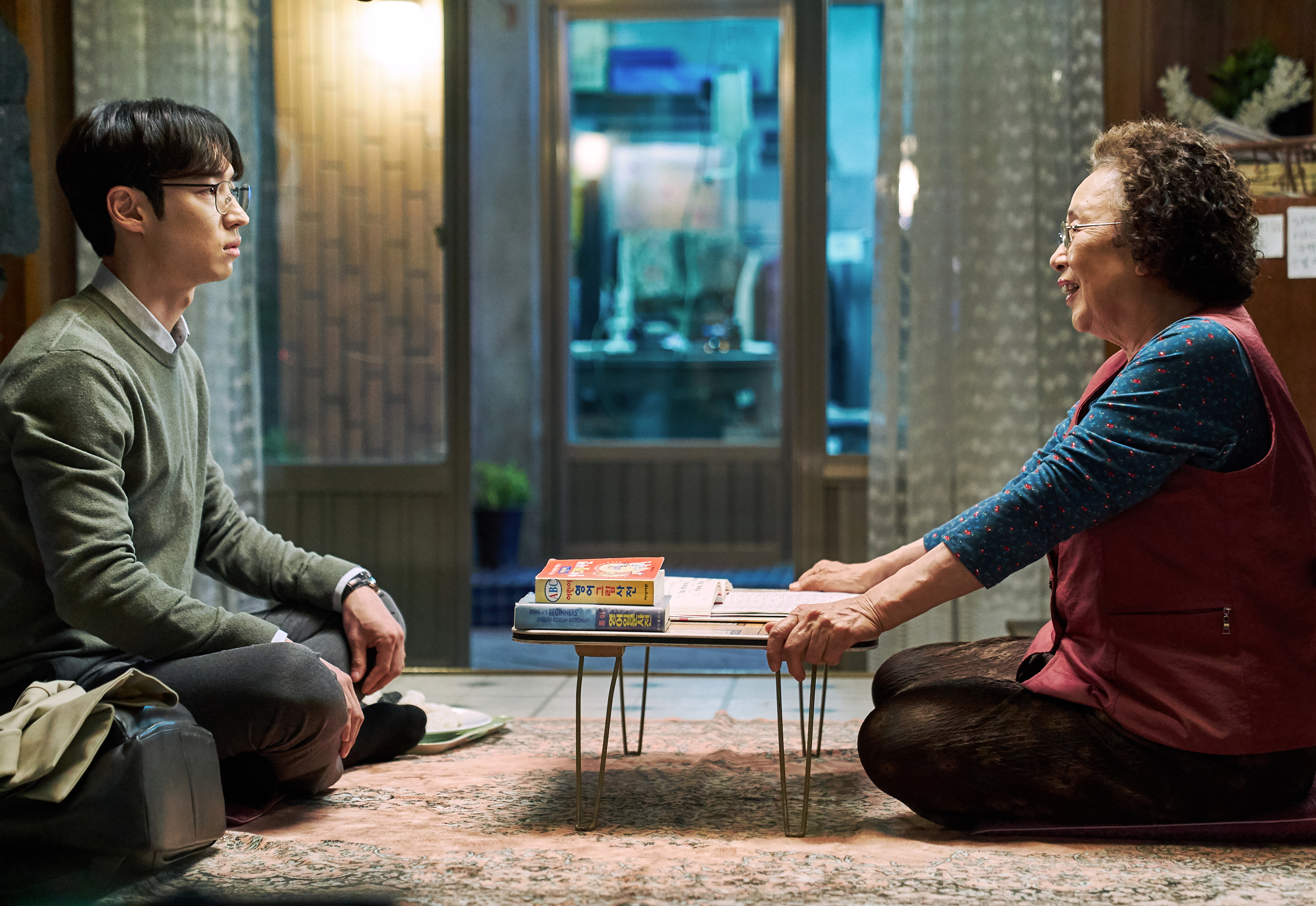 An elderly Korean woman faces a younger man across a low table