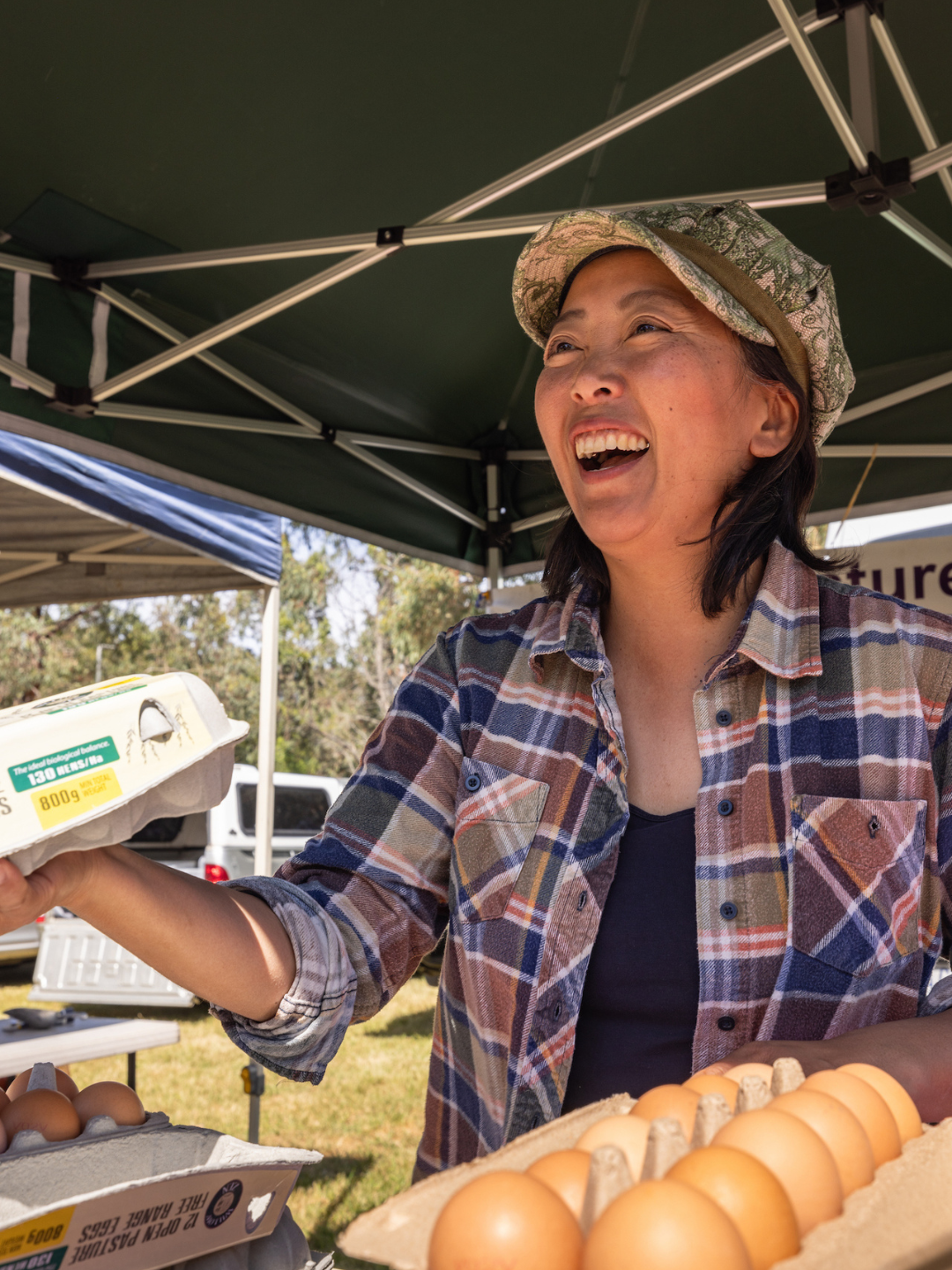 A stallholder wearing a cap and a checkered shirt selling eggs by the dozen.