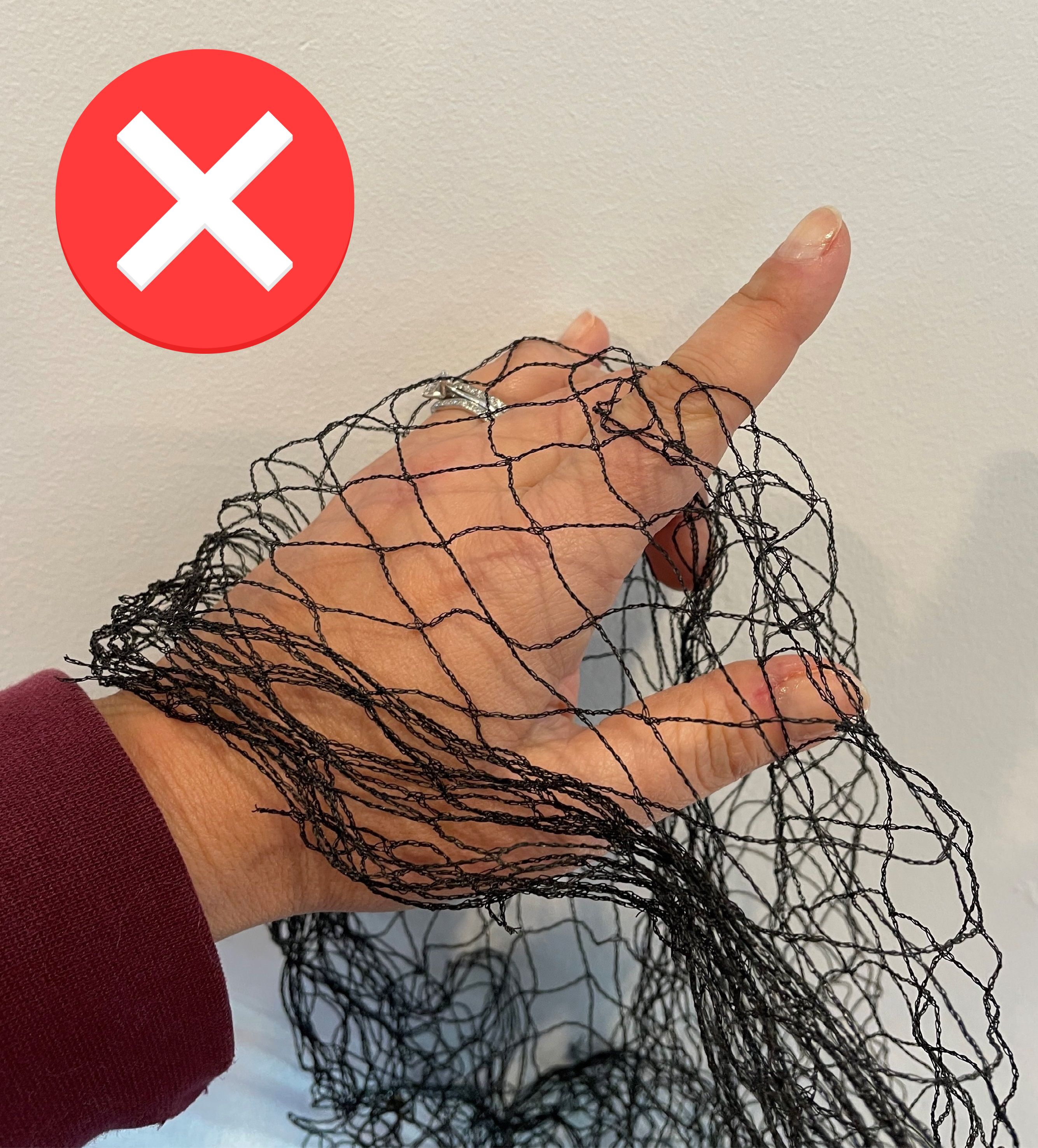 A hand holds netting; there is a cross over the image.