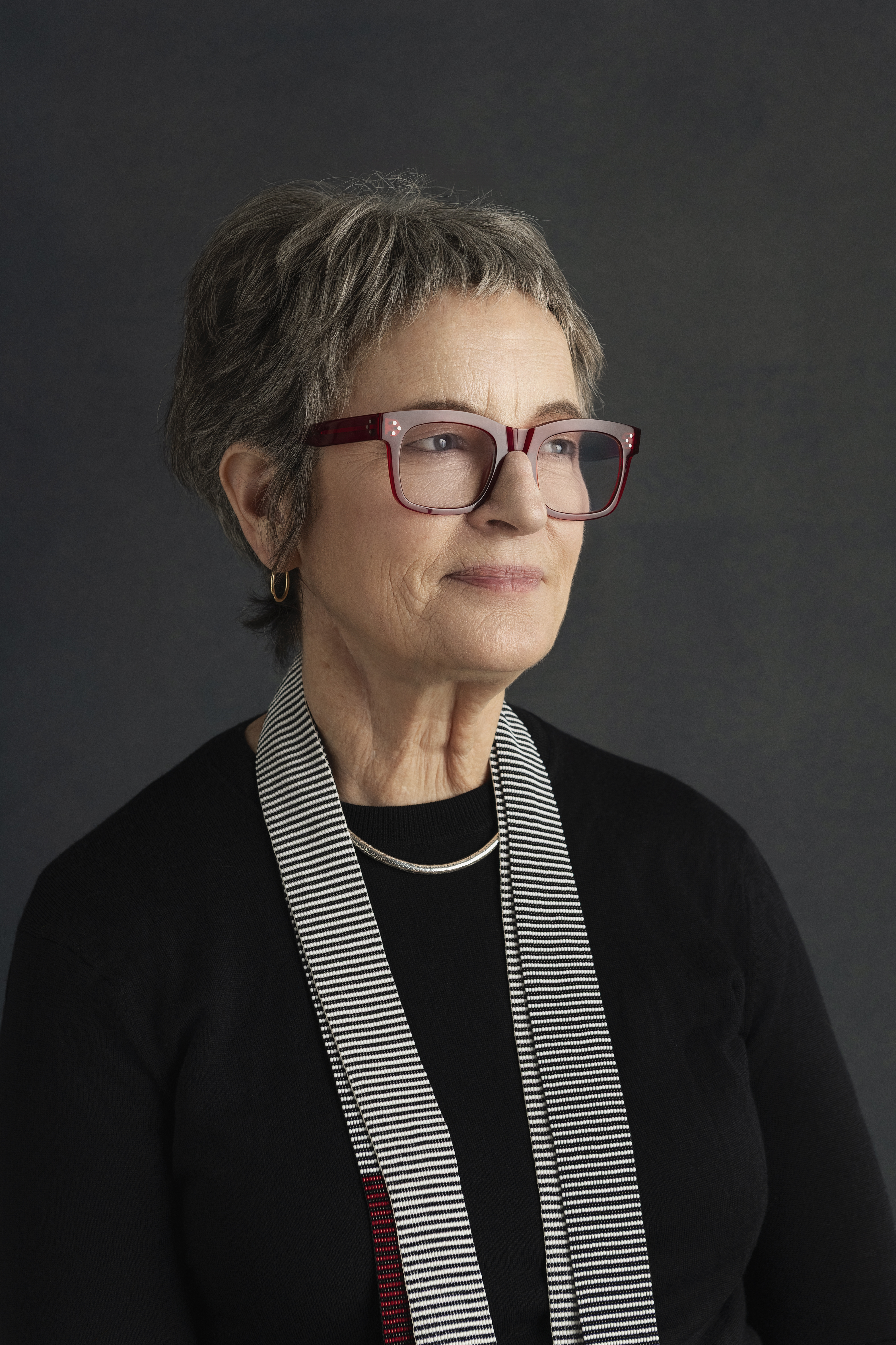 A portrait of a woman wearing glasses and a striped scarf in front of a grey background.