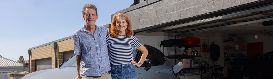 2 adults standing in front of a house smiling at the camera