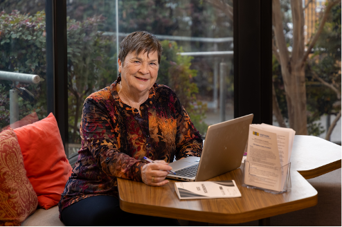 A smiling woman sitting at a table with laptop open