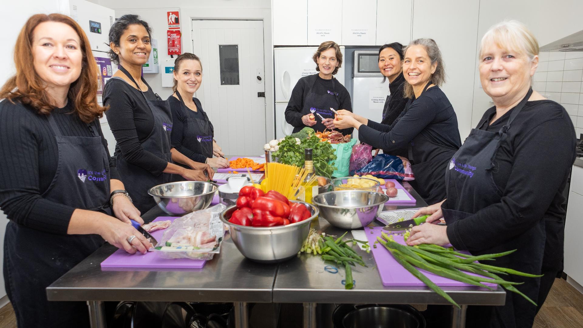 A group of people around an commercial kitchen bench covered in bowls of food