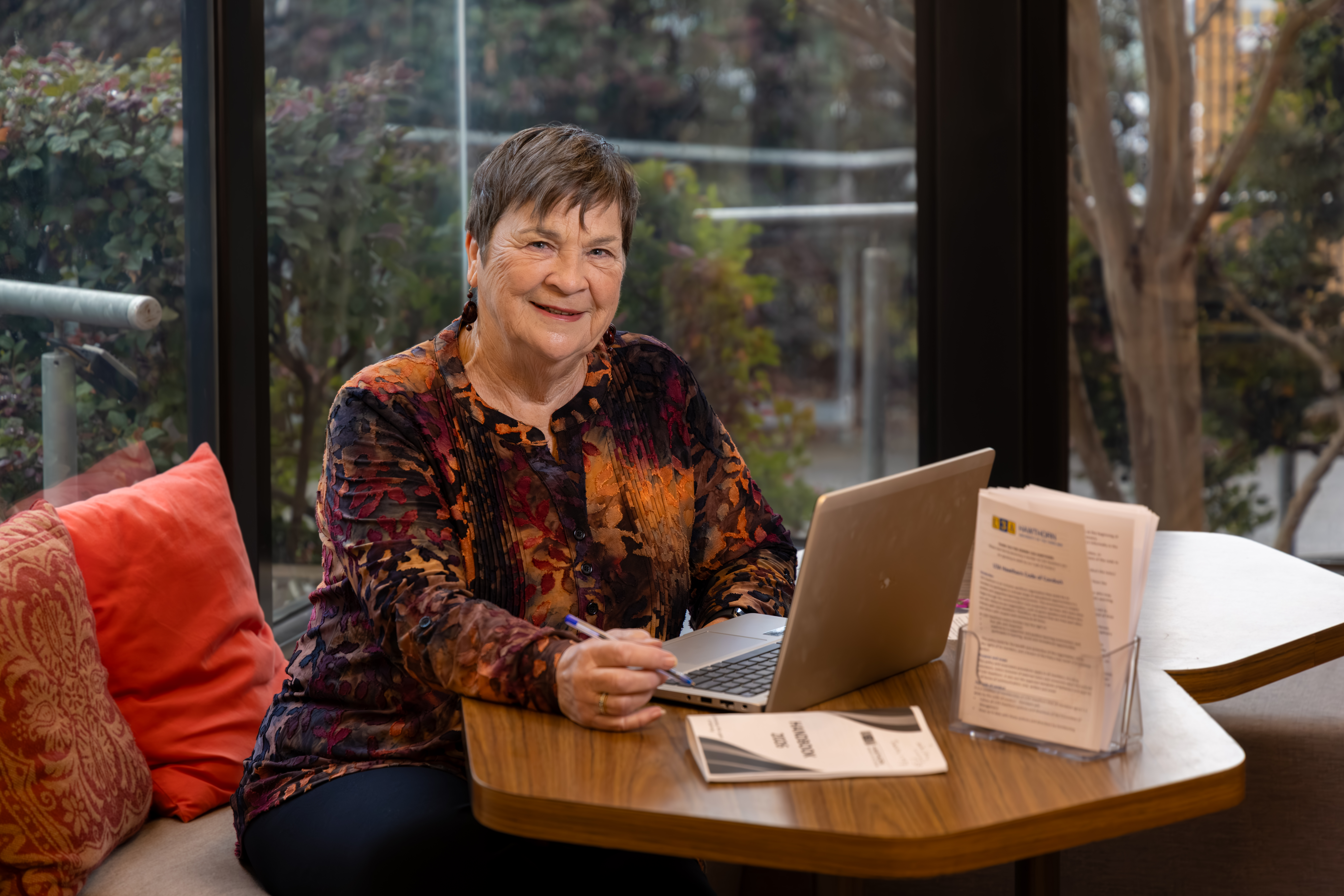 A smiling woman sitting at a table with laptop open