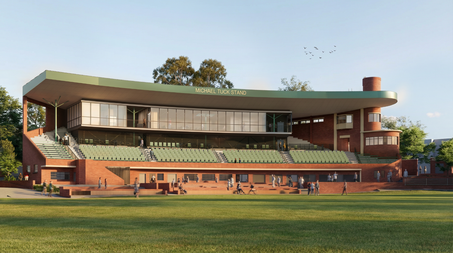 A red brink grandstand with green seats in the middle level. The top level has large glass windows overlooking the ground.