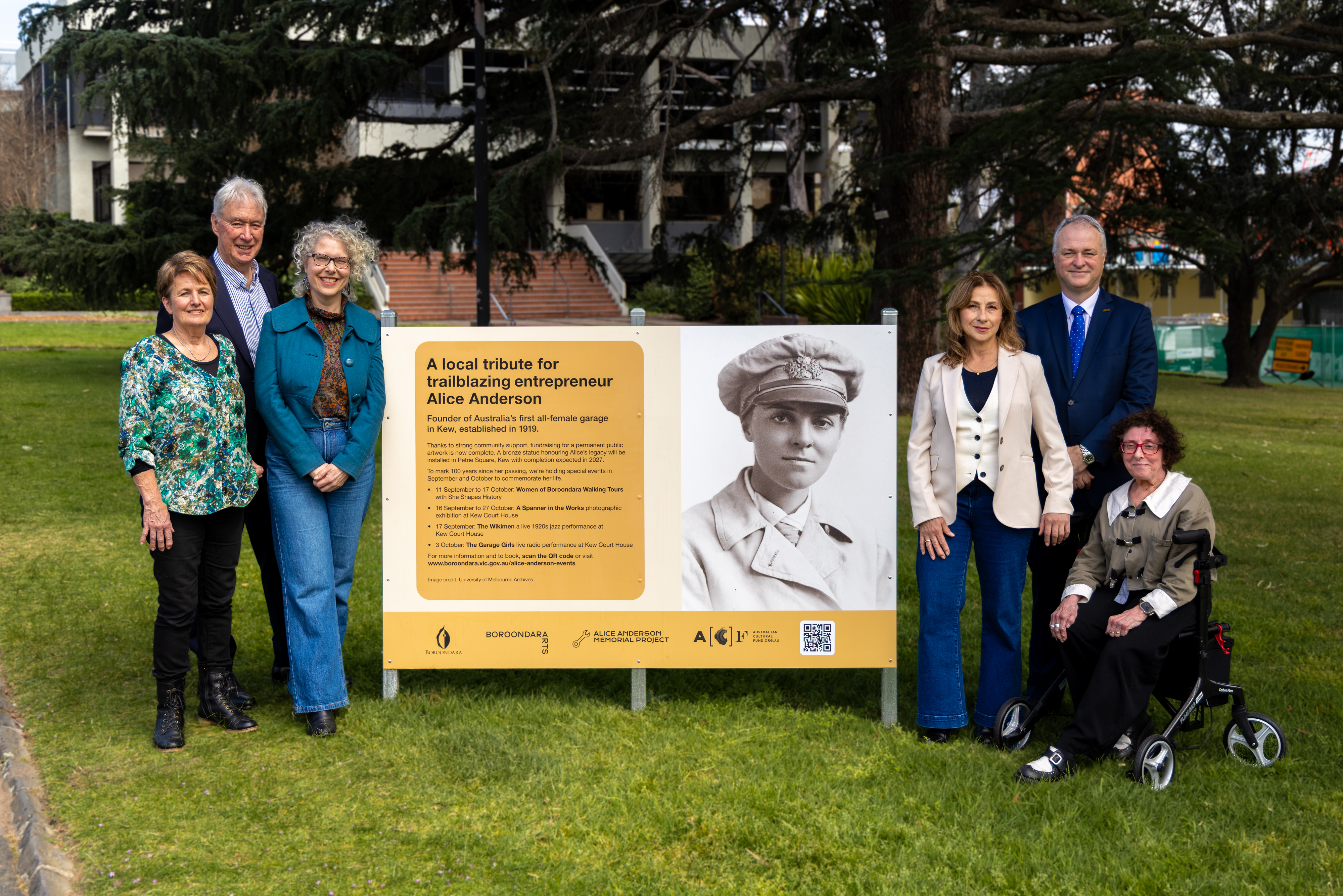 Six people pose beside a sign promoting the Alice Anderson Memorial Project in Kew. To the left of the sign are artist Lis Johnson, Mayor of Boroondara Wes Gault and Alice Anderson Memorial Project co-founder Samantha Lovrich. To the right of the sign are Alice Anderson Memorial Project co-founders Tina Russo (standing) and Loretta Smith (seated), and Victorian Automotive Chamber of Commerce CEO Peter Jones.