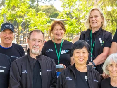 Eight smiling people in matching black uniforms, with trees in the background.